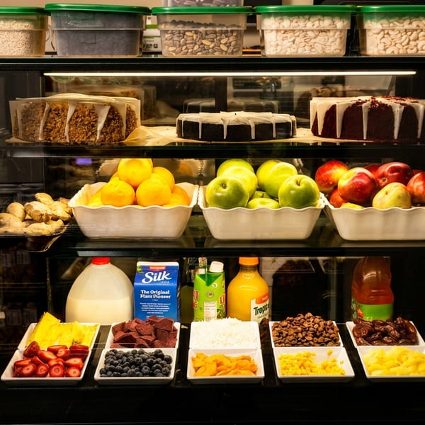 A refrigerated display case filled with cakes, fresh fruit, nuts, and various toppings.