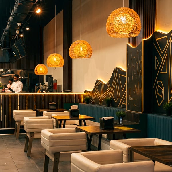 Modern restaurant interior with wicker pendant lights, geometric wall art, and a counter with staff.