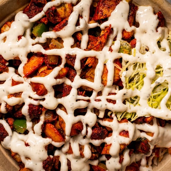 Close-up of a bowl filled with chicken, potatoes, green peppers, lettuce, and white sauce.