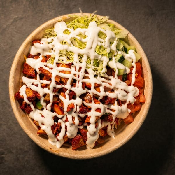 Overhead view of a bowl filled with chicken, lettuce, and white sauce on a dark surface.