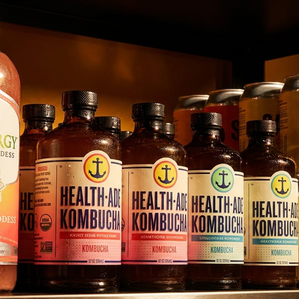 A refrigerated shelf displays various bottled kombucha and canned sodas in different flavors and brands.