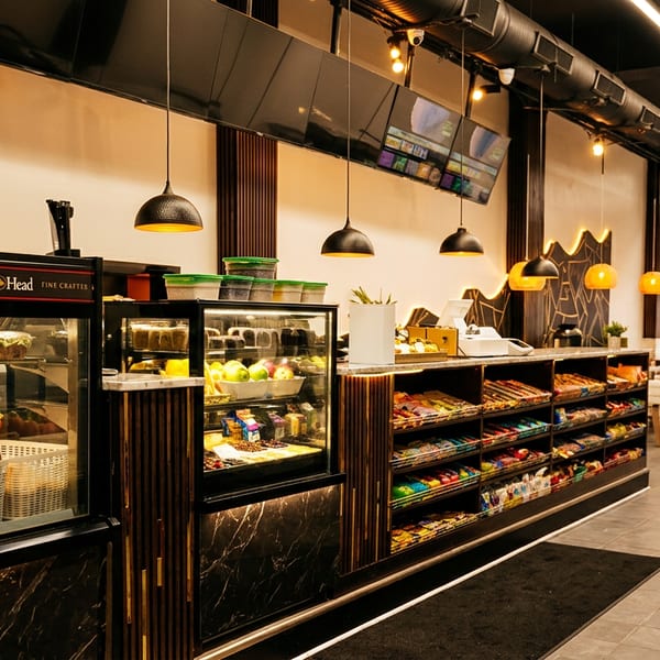 Interior of a modern deli with display cases of food, shelves of snacks, and seating.